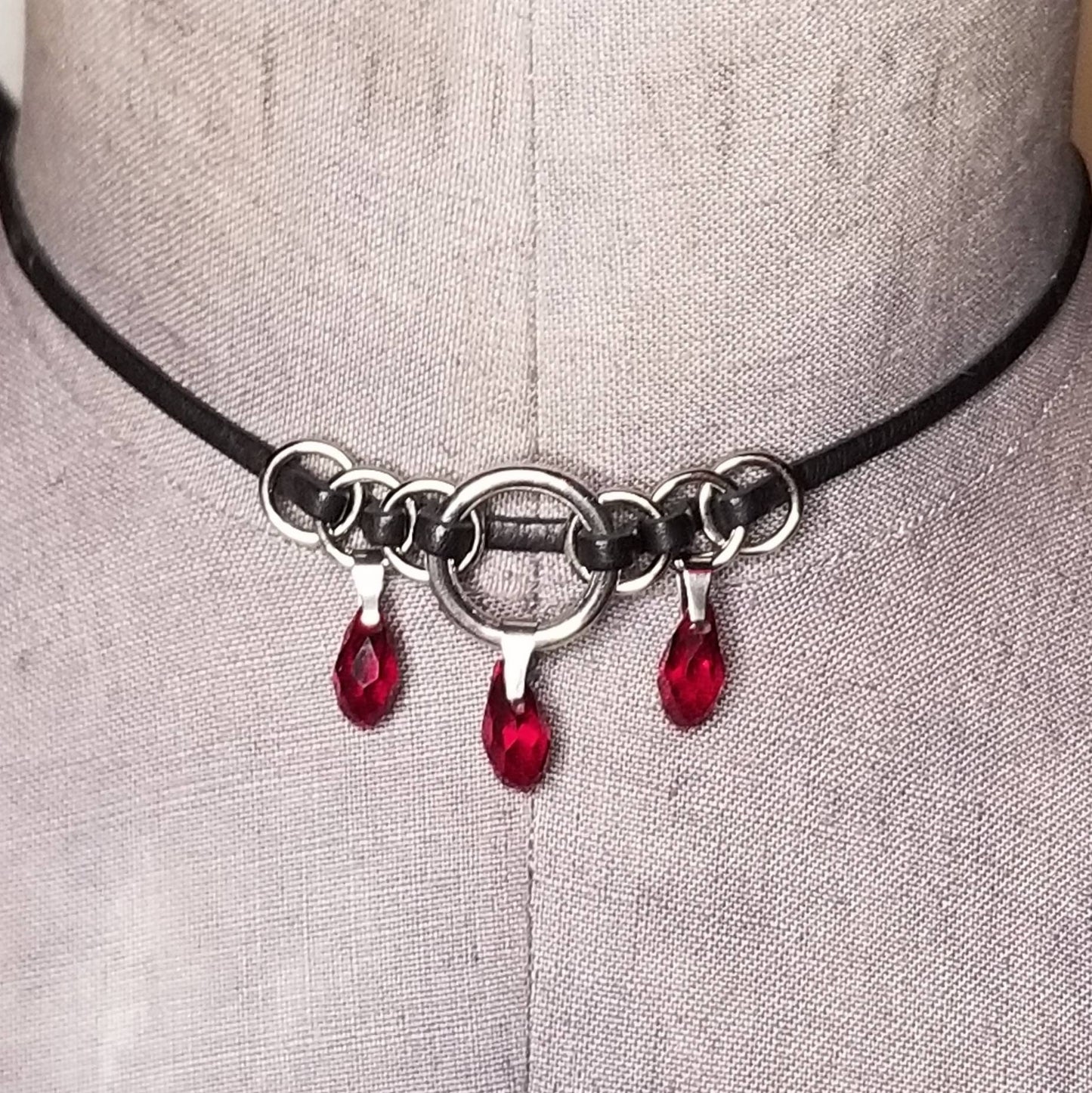 The Delena, red crystal teardrop, and black leather ribbon necklace. Leather is handwoven through silver orings with red teardrops.
