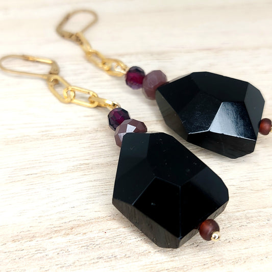 Chunky black geometric drop earrings with gold chain and purple bead detail.
