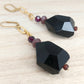 Chunky black geometric drop earrings with gold chain and purple bead detail.