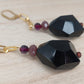 Chunky black geometric drop earrings with gold chain and purple bead detail.