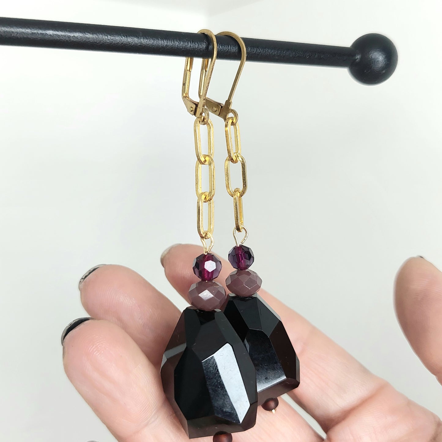 Chunky black geometric drop earrings with gold chain and purple bead detail.