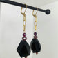 Chunky black geometric drop earrings with gold chain and purple bead detail.